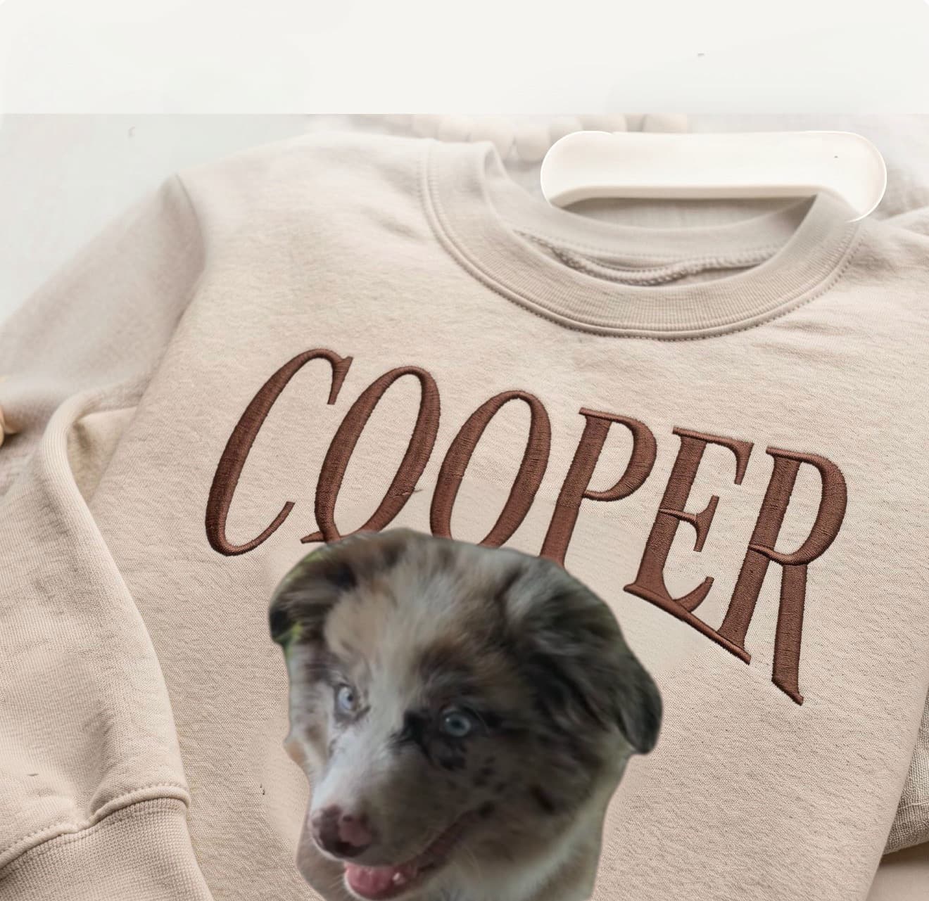Beige sweatshirt featuring brown embroidered 'COOPER' text and a blue-eyed merle puppy face.