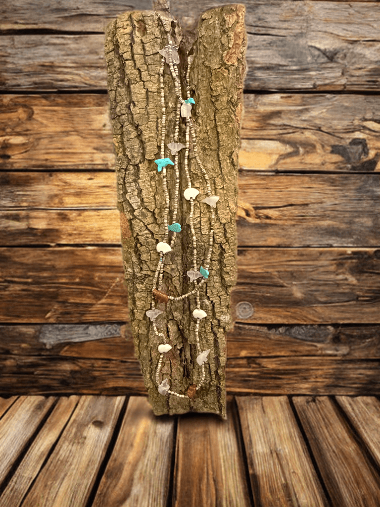 Multi-strand heishi bead necklace with animal stone charms draped over rough tree bark.